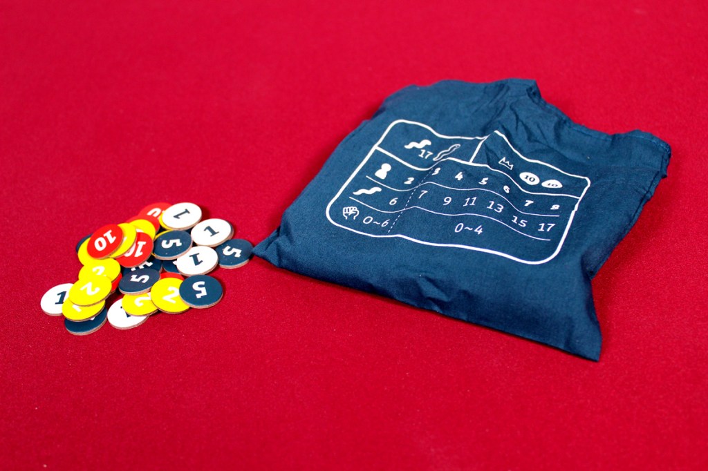 A blue fabric pouch with a diagram printed on it, next to a pile of colorful game tokens with numbers on them, all set against a red background.