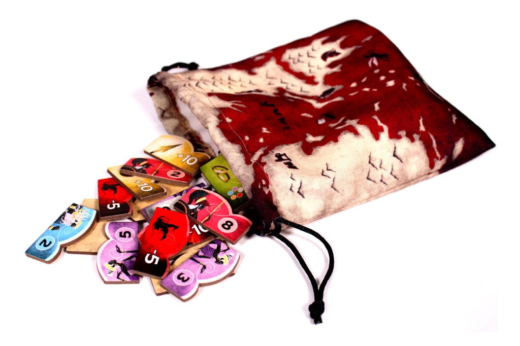 A fabric bag with a colorful design contains various gaming tokens laid out beside it. The tokens feature different colors and numbers, suggesting they are part of a board game.