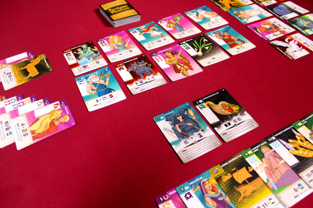 A tabletop game setup featuring a variety of fantasy-themed playing cards on a red surface, with detailed illustrations and text on each card.